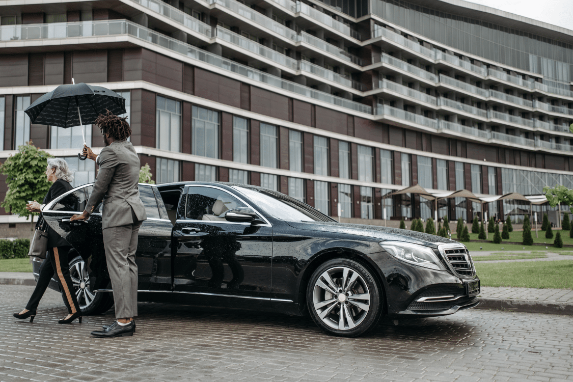 Chauffeur opening car door and holding umbrella over passenger